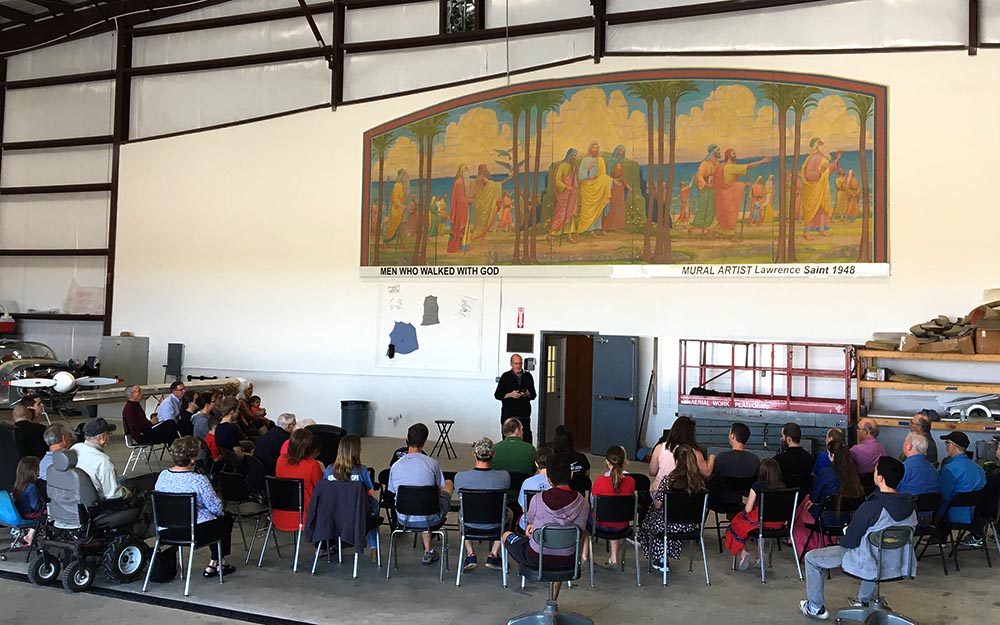 ITEC team gathered in hangar in front of mural